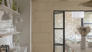 A modern kitchen with white cabinetry, a dining area with a stone wall, and a large window.