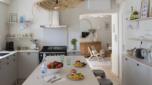 A modern kitchen with white cabinets, a central island with food, a hanging light, and a rustic ceiling.