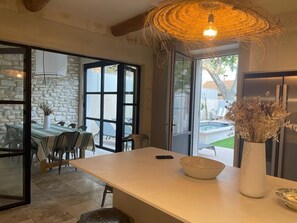 A modern kitchen with a large island, a dining area with a table and chairs, and a view of a pool outside. - MAISON EN PLEIN COEUR DU VILLAGE  (Maussane-les-Alpilles)