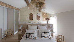 A bedroom with a large bed, a wooden headboard, a hanging light fixture, and a stone wall with a mirror.