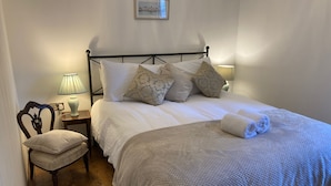 A neatly made bed with a white comforter and several pillows, a wooden nightstand with a lamp, a chair, and a fluffy rug. - Mill Villa: stunning 4 bed retreat 5 mins from Pakefield’s beautiful sandy beach (Lowestoft)