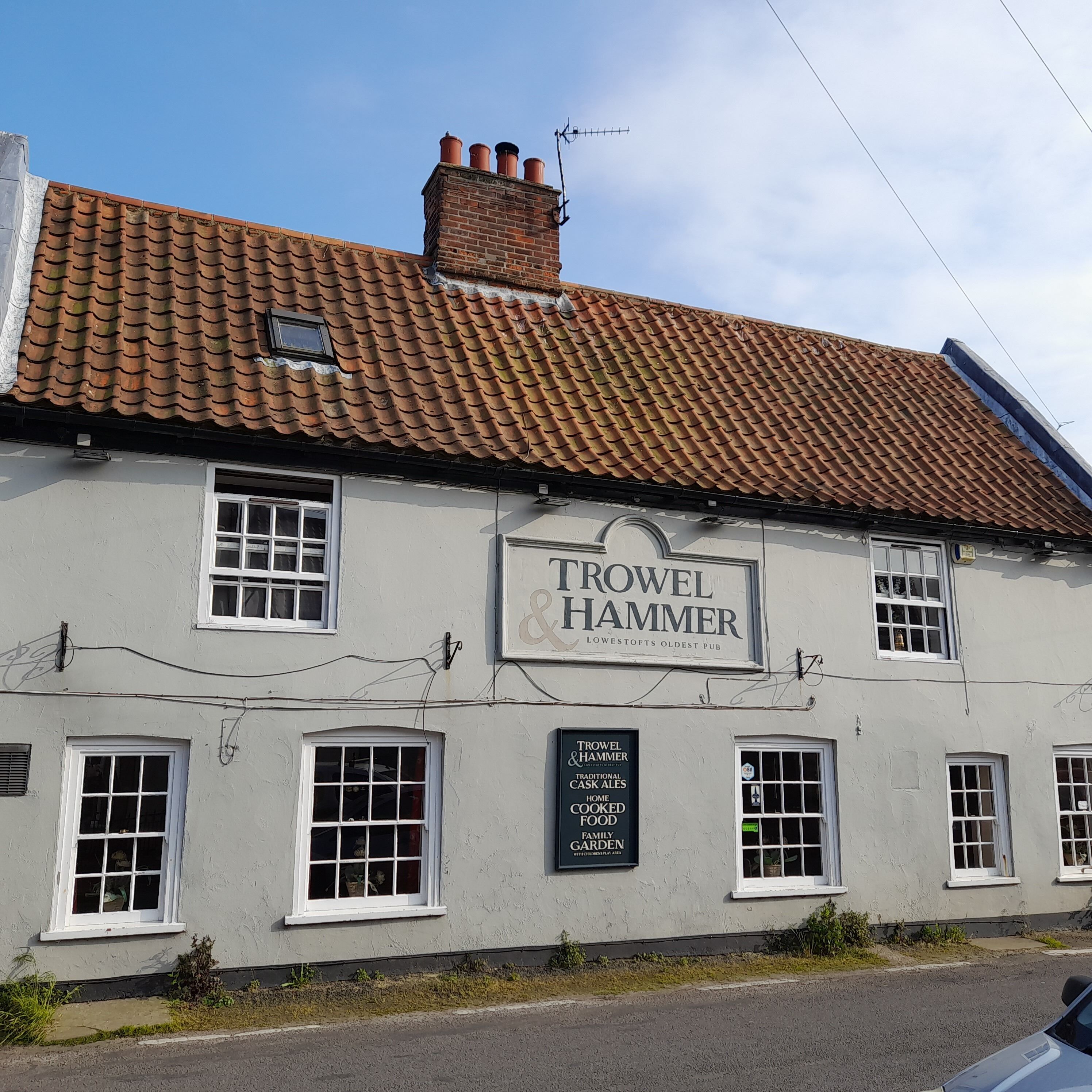 A building with a sign reading "Trowel & Hammer" and a smaller sign below stating "Traditional Cask Ales, Home Cooked Food, Family Garden".