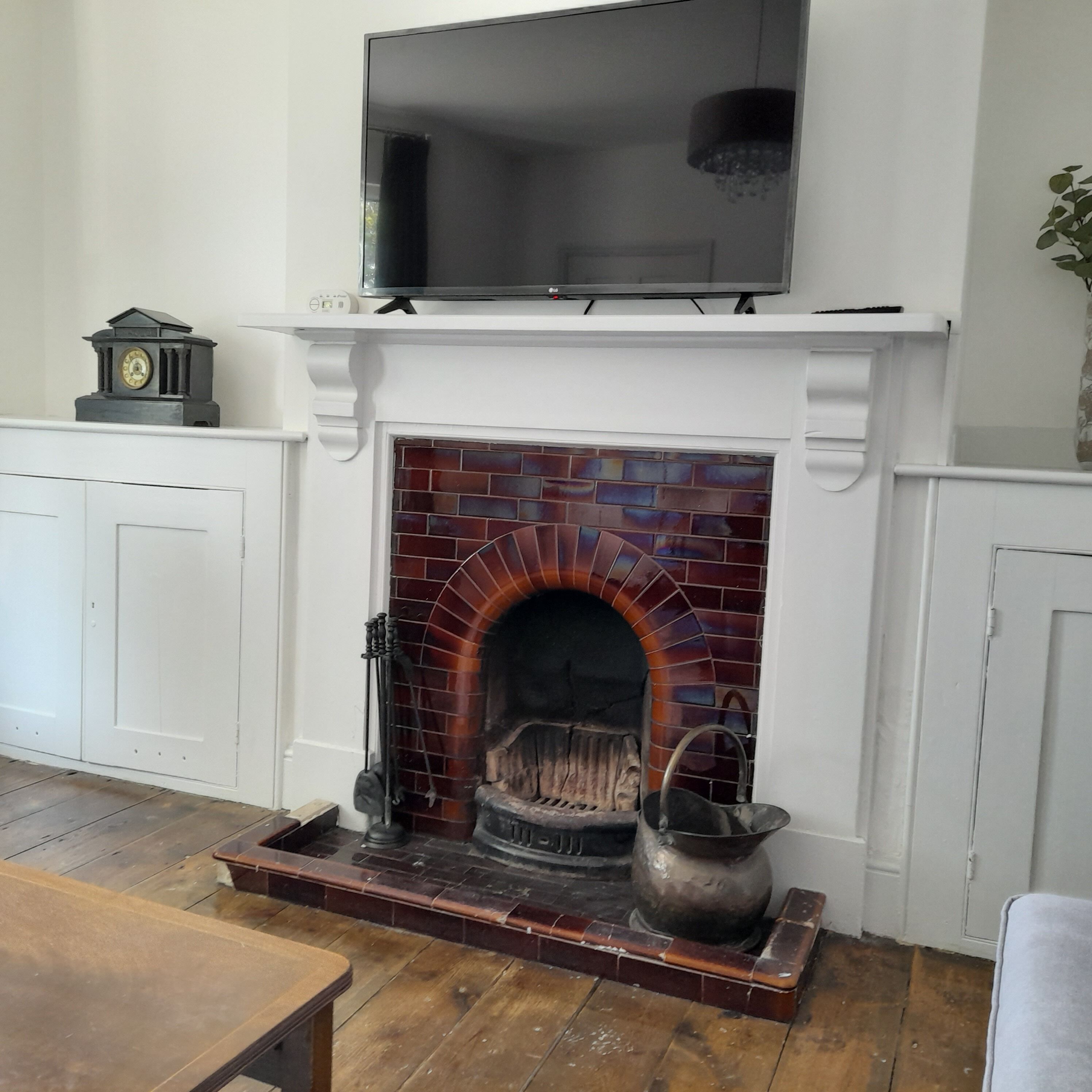 A fireplace with a TV above it, a clock on the left, and a plant on the right.
