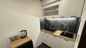 Une cuisine compacte avec des meubles blancs, un plan de travail noir, une cuisinière encastrée et un évier.