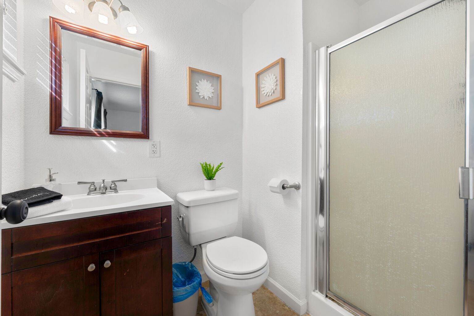 Une salle de bain avec un meuble-lavabo en bois, des toilettes blanches, un espace douche et deux éléments décoratifs encadrés accrochés au mur.