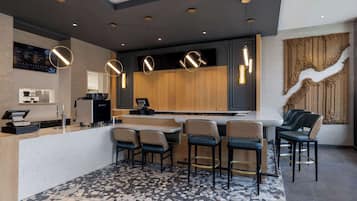A modern kitchen with a central island, bar stools, pendant lighting, and a digital menu board.