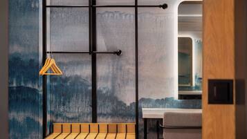Ein modernes Interieur mit einer Holzbank, einem Metallgestell mit einem aufgehängten Kleidungsstück und Blick auf eine gebirgige Landschaft durch eine strukturierte Wand.