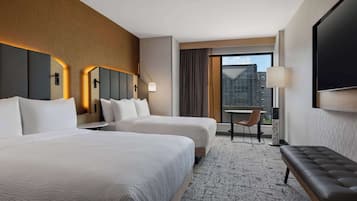 Une chambre d’hôtel avec deux lits, un banc, un bureau et une grande fenêtre donnant sur la ville.