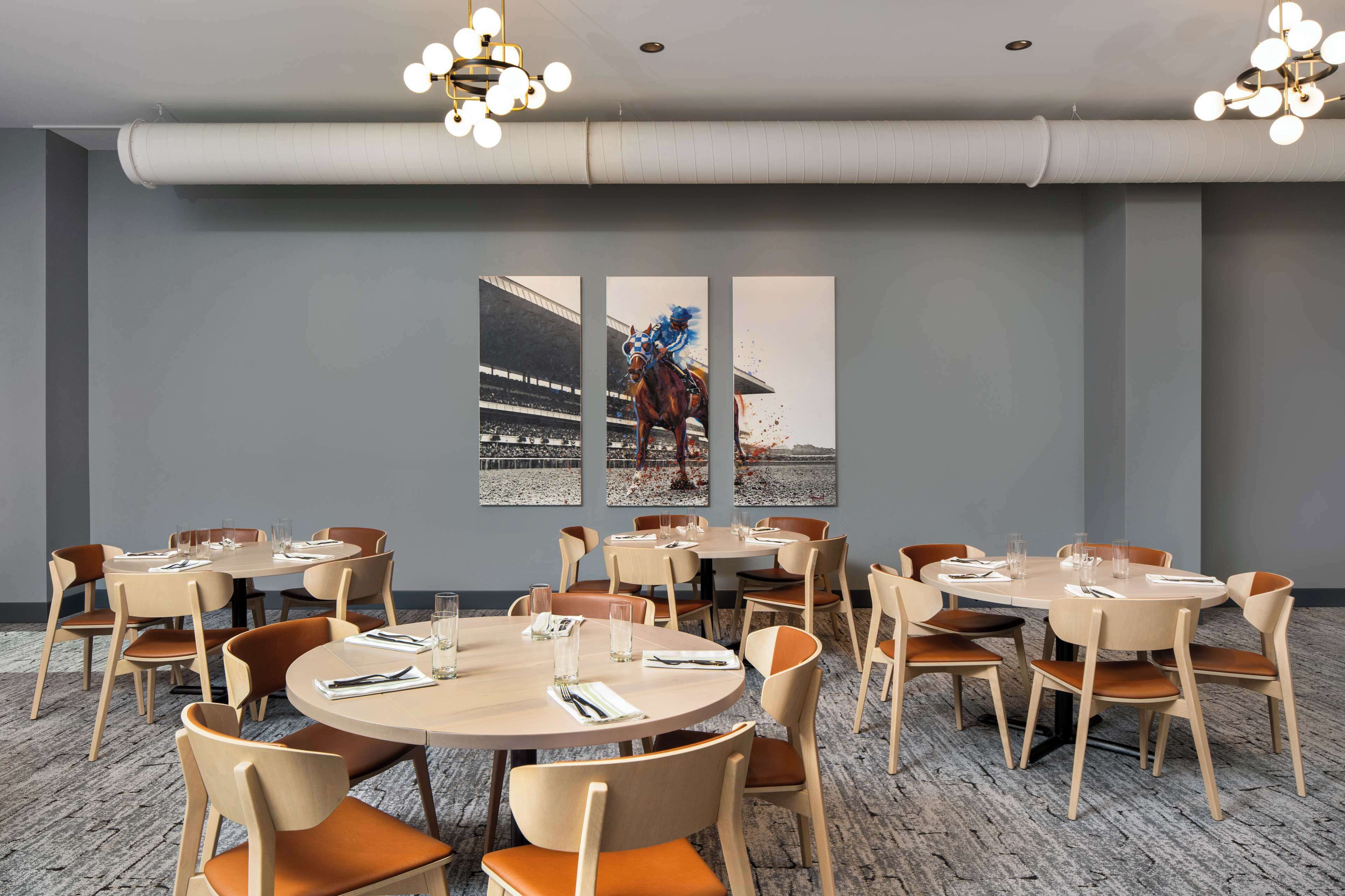 A conference room with round tables and chairs, a large window with a view of a horse race, and a chandelier.