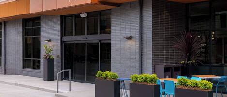 Exterior de un hotel con diseño moderno, que presenta un letrero que dice "TEMPO by Hilton" y la dirección "710". Hay áreas de estar al aire libre con mesas y sillas, y macetas con plantas.