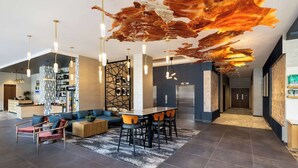 A modern hotel lobby with a reception desk, seating area, and a large abstract ceiling artwork. - Tempo By Hilton Louisville Downtown Nulu (Louisville)