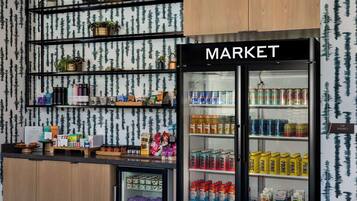 Un espacio comercial con estantes llenos de diversos productos, un expositor refrigerado con bebidas, y un letrero que dice "MARKET".