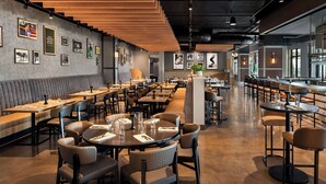 A modern restaurant with high tables and booths, wooden ceiling panels, and framed pictures on the walls. - Tempo By Hilton Louisville Downtown Nulu (Louisville)