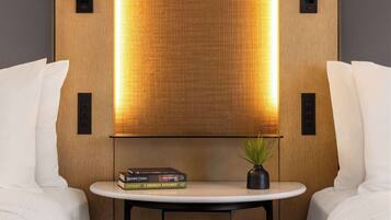 Ein modernes Hotelzimmer mit einer Wandpaneele aus Holz, einem kleinen runden Tisch mit Büchern und einer Pflanze sowie zwei schwarzen, an der Wand montierten Lichtschaltern.