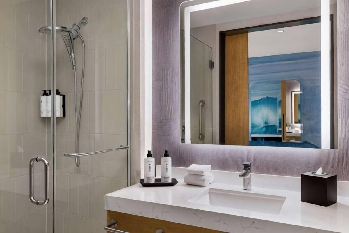 A modern bathroom with a glass shower enclosure, a white vanity with a large mirror, and a view of a mountain through the window.