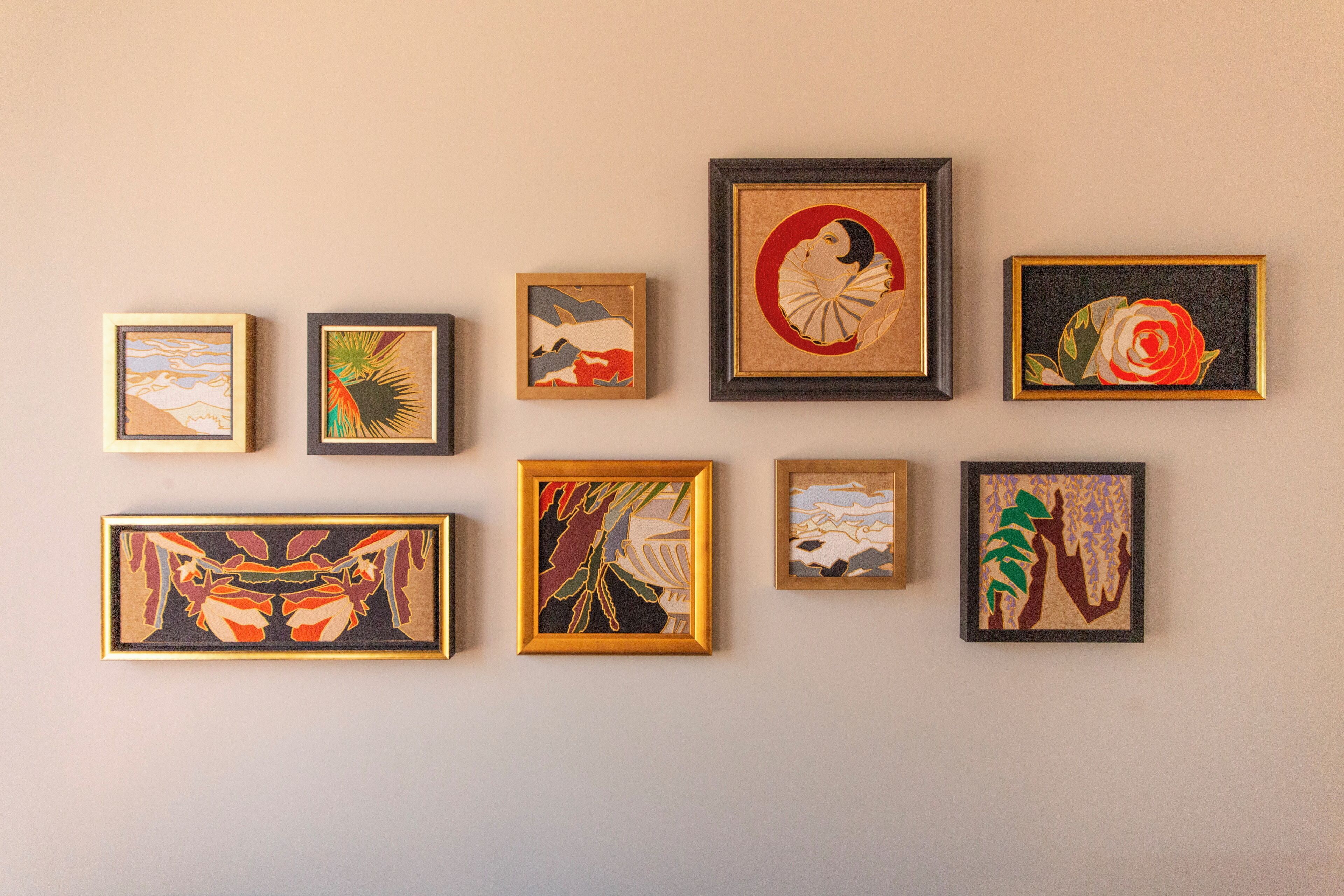 Eine Wand mit acht gerahmten Kunstwerken unterschiedlicher Stilrichtungen und Motive.