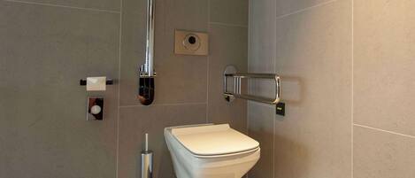 Un baño moderno con inodoro blanco, secamanos y barra de apoyo.