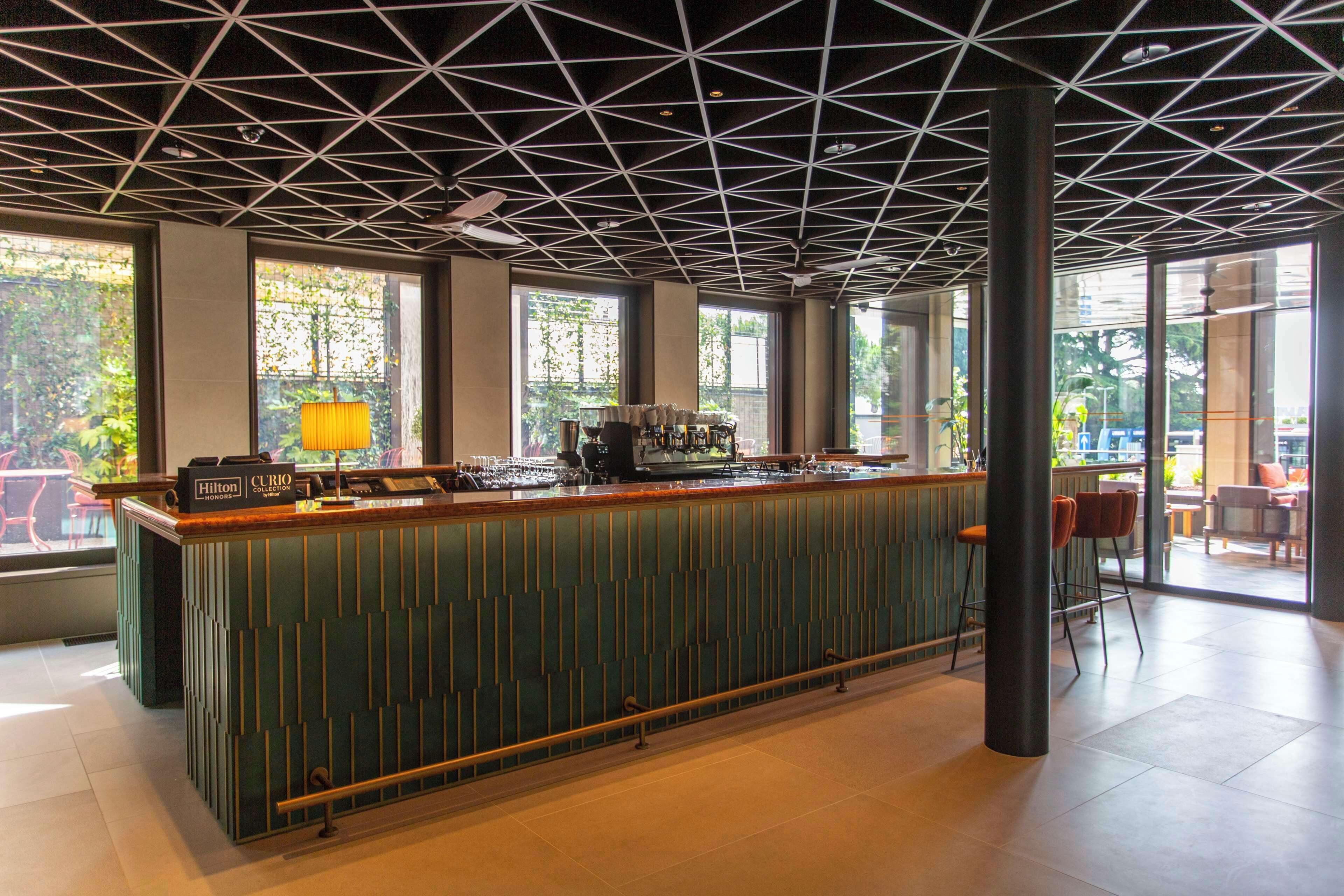 Een moderne bar met een groene toog, een koffieapparaat en een zithoek met stoelen en tafels.