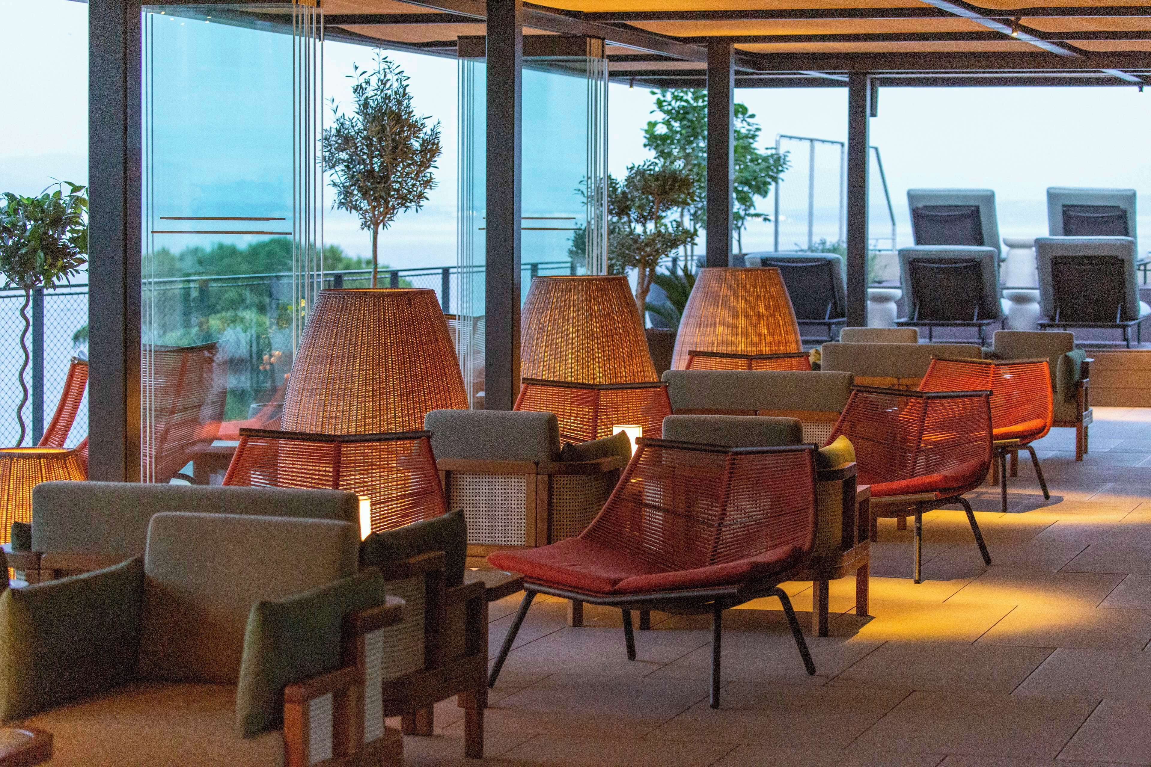 A terrace with wicker chairs and tables, large windows, and a view of the sea.
