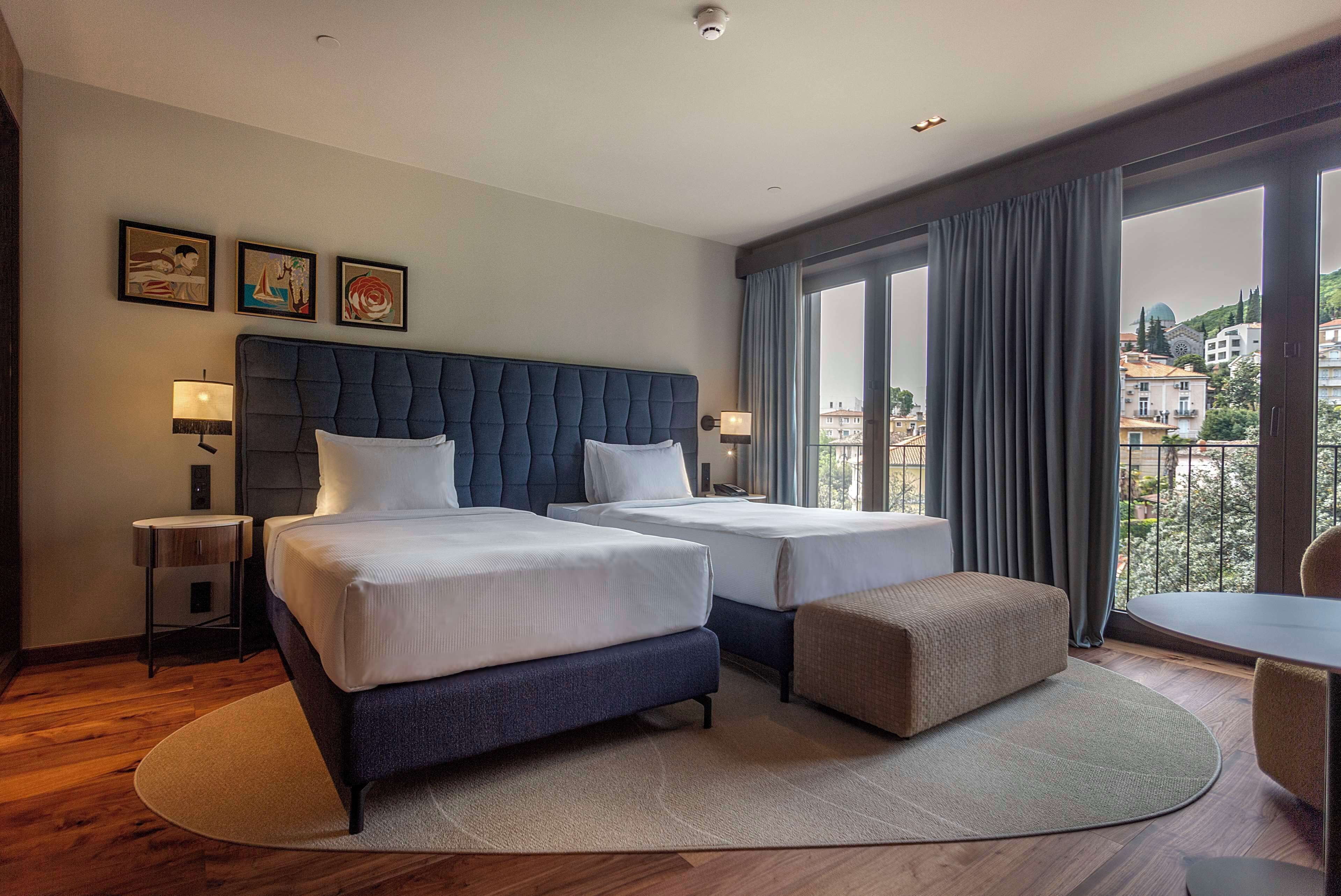 A hotel room with two beds, a sofa, a dining table, and a view of the city.
