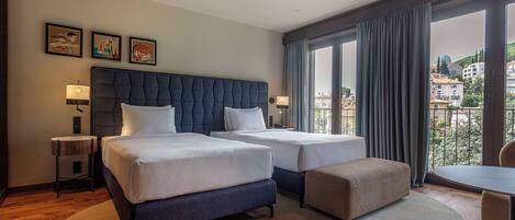 A hotel room with two beds, a sofa, a dining table, and a view of the city.