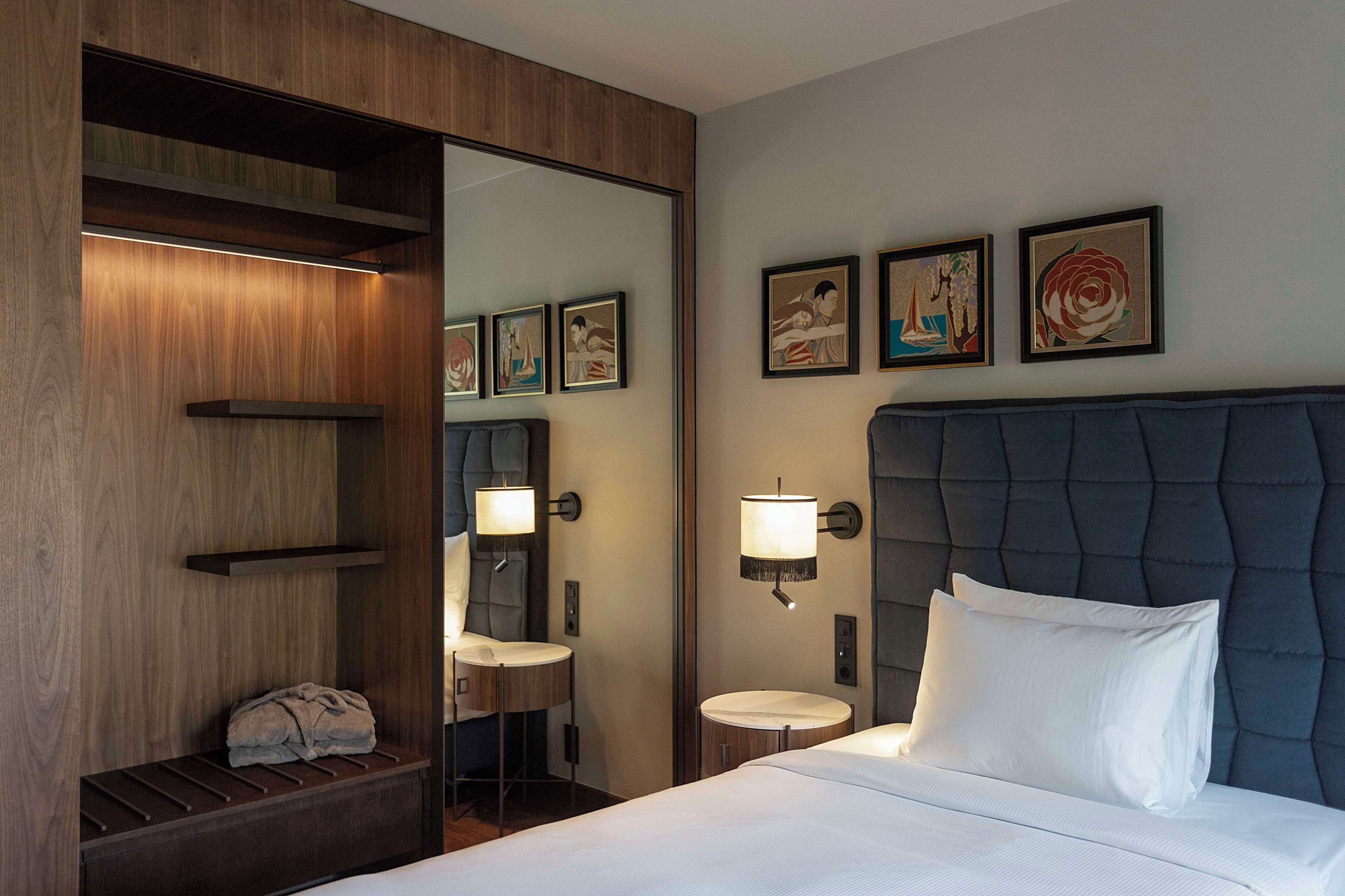 Ein Hotelzimmer mit einem Bett, einem Schminktisch mit Spiegel, einer Wandlampe und einem Kunstwerk an der Wand.