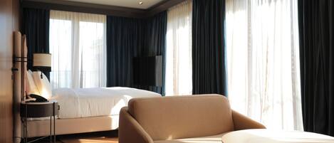 A hotel room with a bed, a chair, a small table, a TV, and curtains.