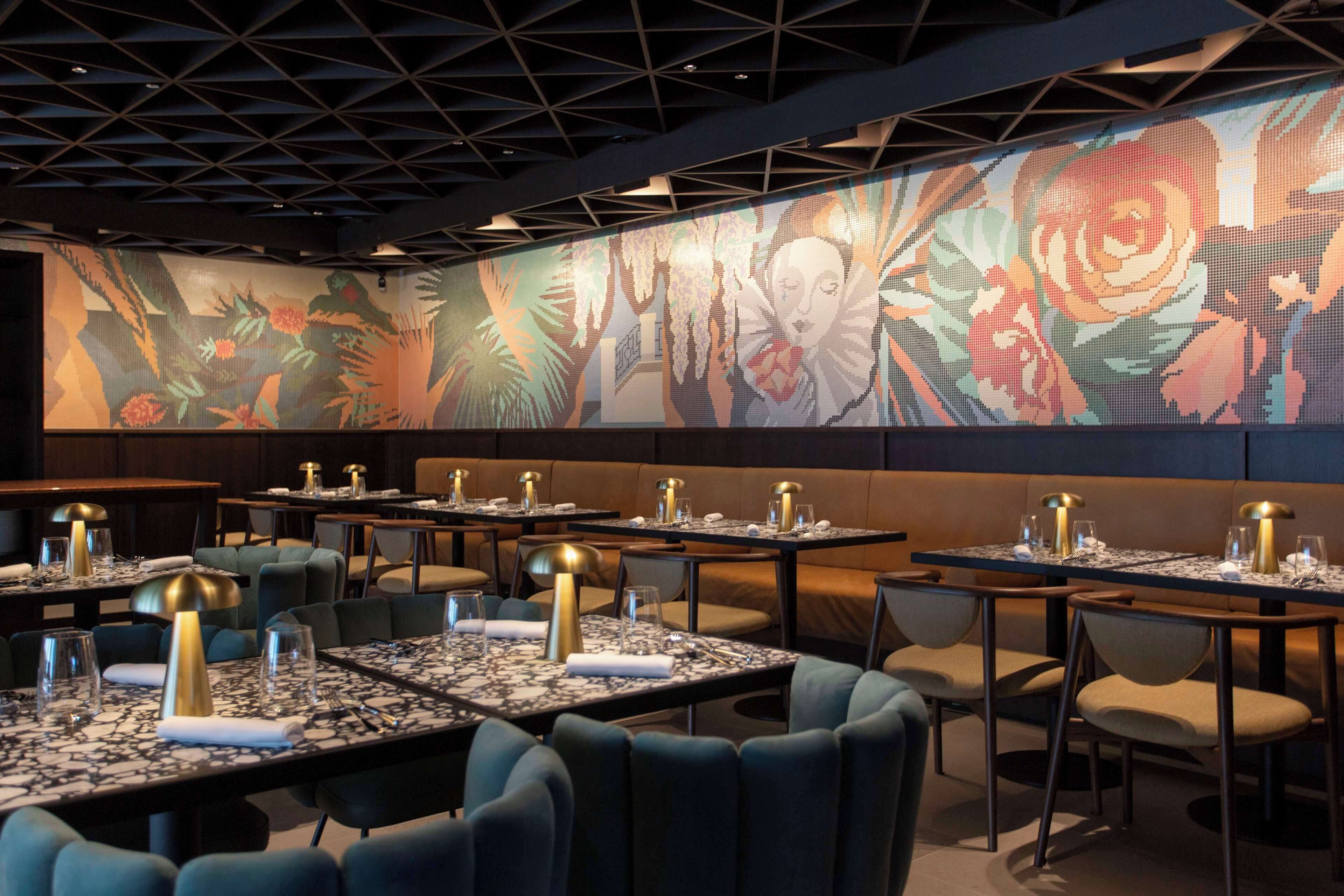 A restaurant with tables set for dining, featuring a large floral mural on the wall.