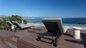 A deck with lounge chairs and a small table, overlooking a pool and the sea. - Keight Hotel Opatija, Curio Collection By Hilton (Opatija)