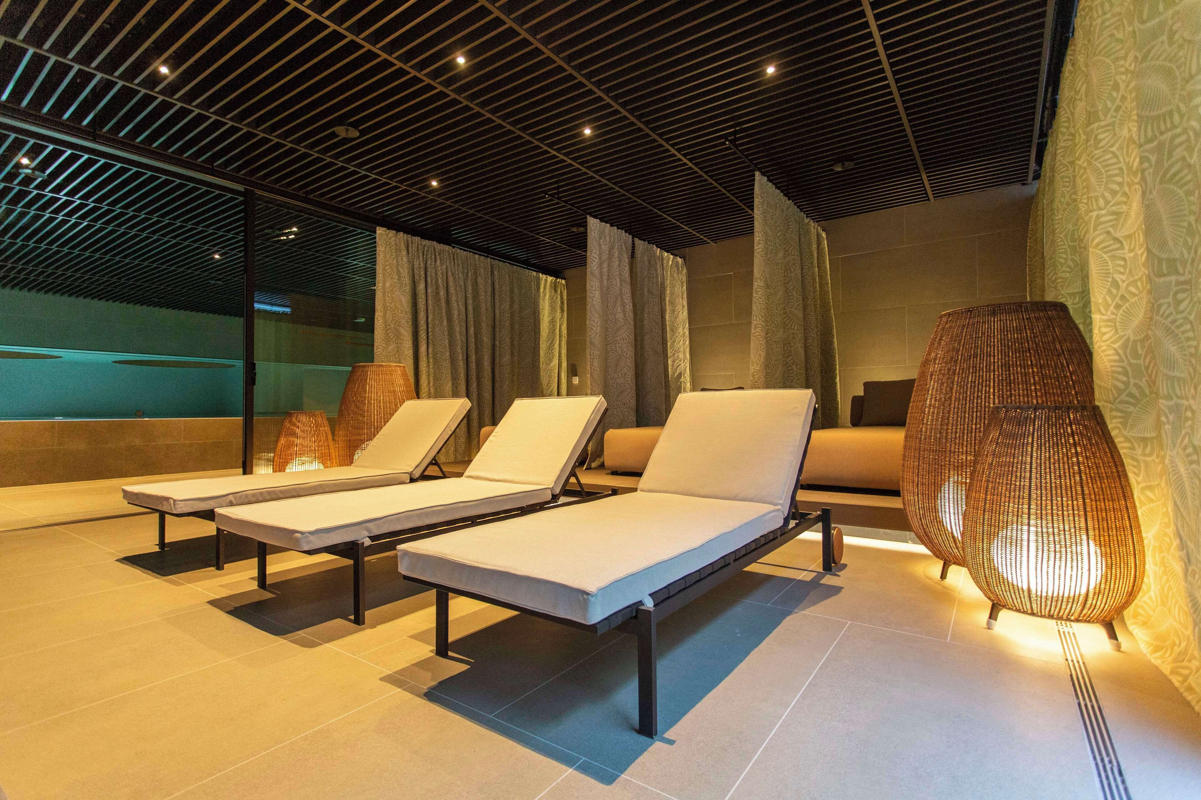 Un área interior moderna para relajarse, con sillones, un muro decorado y un techo con iluminación lineal.