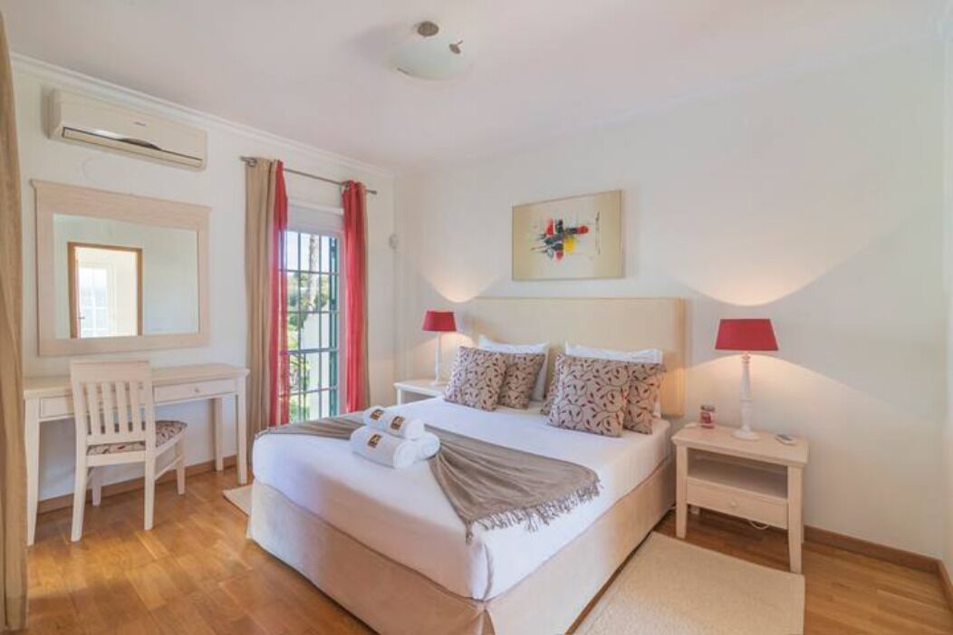 A bedroom with a bed, a desk, a chair, and a nightstand.
