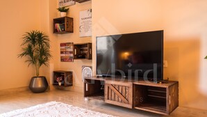 Una sala de estar con una televisión de pantalla plana sobre un soporte de madera, una planta en maceta y una alfombra blanca.