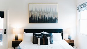 A bedroom with a large bed, two bedside tables with lamps, a painting above the bed, and a window with patterned curtains. - Modern Cabin, close to marina and downtown Blue Ridge (Blue Ridge)