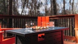 An outdoor grill with a clear glass enclosure, set on a black metal table, surrounded by red chairs, with a wooden deck and trees in the background. - Modern Cabin, close to marina and downtown Blue Ridge (Blue Ridge)