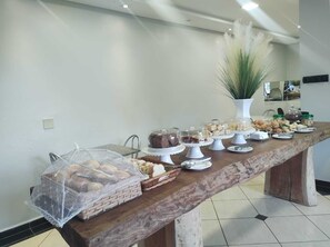 A buffet table with various food items, including cakes and pastries, in a modern setting with a marble countertop and a decorative plant.