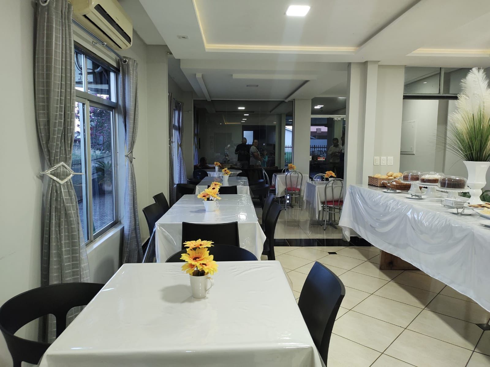 A dining area with tables covered in white tablecloths, chairs, and flower centerpieces.