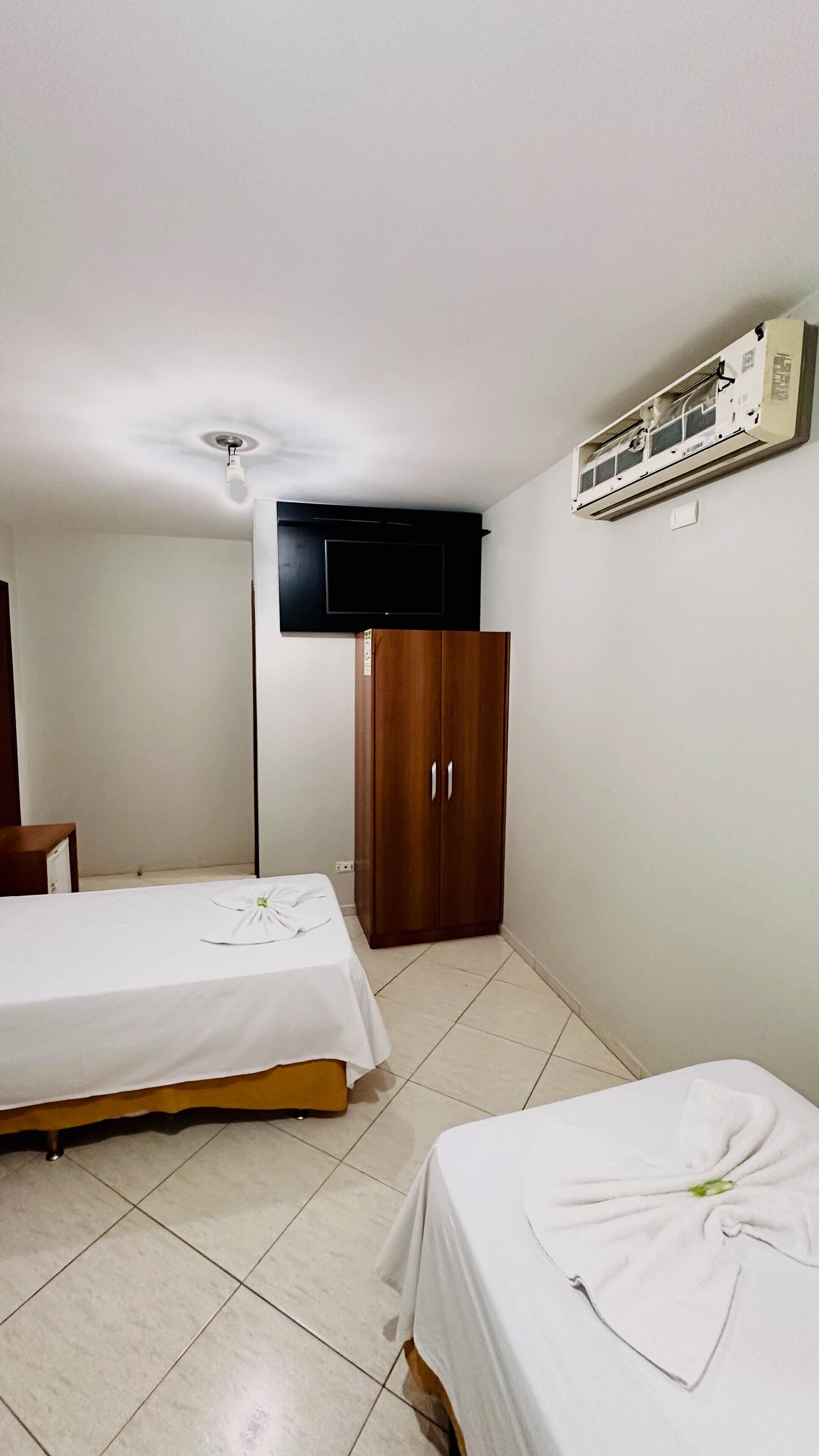 A small, clean room with two beds, a wardrobe, a flat-screen TV, and an air conditioning unit.