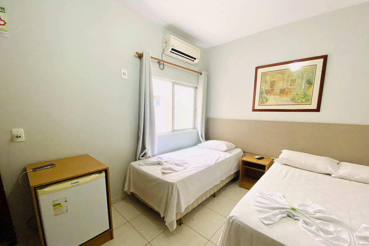Habitación de hotel con dos camas, un escritorio pequeño, un refrigerador y una ventana con cortinas.