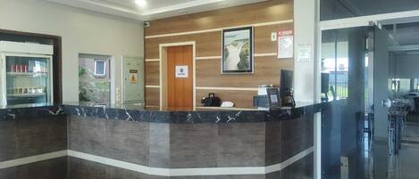 Una zona de recepción con mostrador de mármol, paneles de madera, un cuadro enmarcado y un puerta de cristal que da a un comedor.