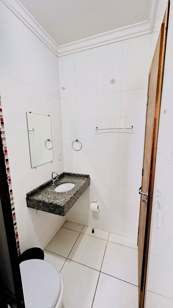 A bathroom with a granite countertop sink, a mirror, a towel ring, and a shower area.