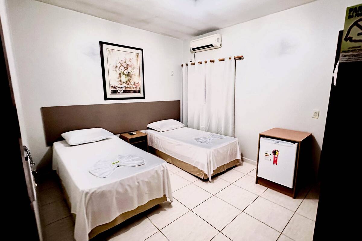 Habitación de hotel con dos camas, un refrigerador pequeño, aire acondicionado y un cuadro en la pared.