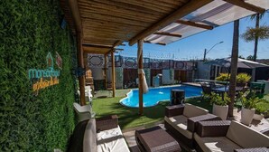Un espace aménagé au bord de la piscine, avec des meubles en osier, une piscine et un mur végétal agrémenté d'une enseigne au néon.