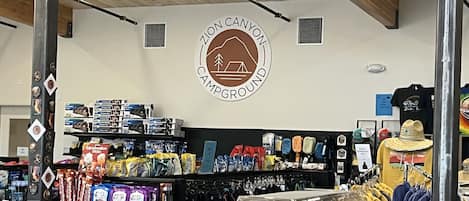 Un magasin avec une enseigne indiquant « Camping », des étagères remplies d’en-cas et un portant à vêtements.