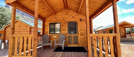 A wooden cabin with a covered porch, two chairs, and a window.
