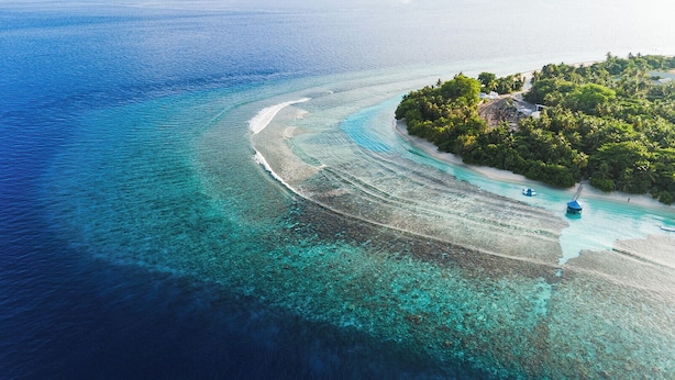 Vista aérea de una isla tropical con aguas turquesas cristalinas, una playa de arena y abundante vegetación.