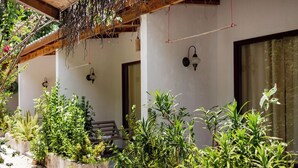 Un espacio al aire libre cubierto con plantas en macetas, un banco de madera y una lámpara fijada a la pared.