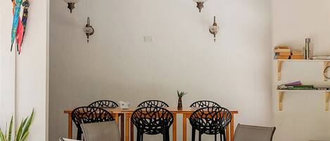 A covered outdoor dining area with a round table, four chairs, a ceiling fan, and wall-mounted lights.
