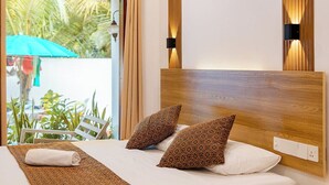 Una habitación de hotel moderna con un cabecero de madera, dos almohadas estampadas, una colcha blanca y una mesita de noche de madera.