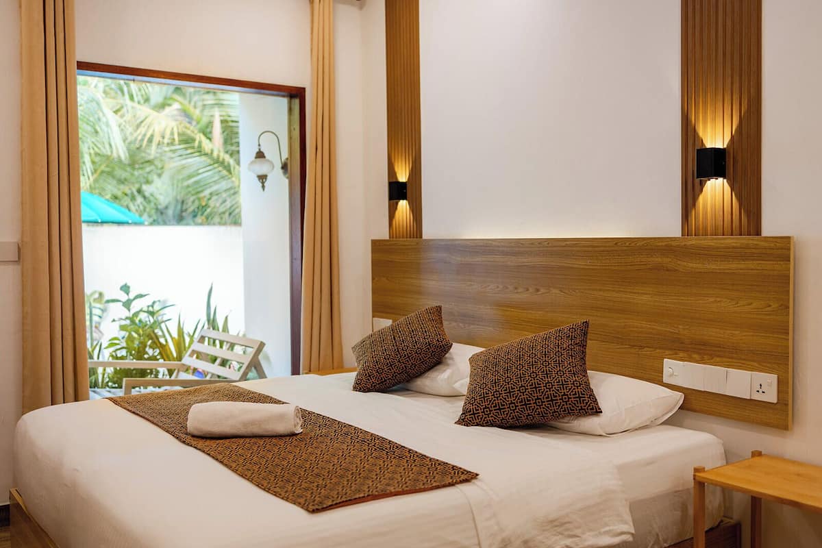 A neatly made bed with patterned pillows, a wooden headboard, and two wall-mounted lights.