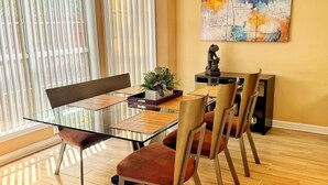 Un comedor con mesa de vidrio, sillas marrones, piso de madera y un cuadro en la pared.